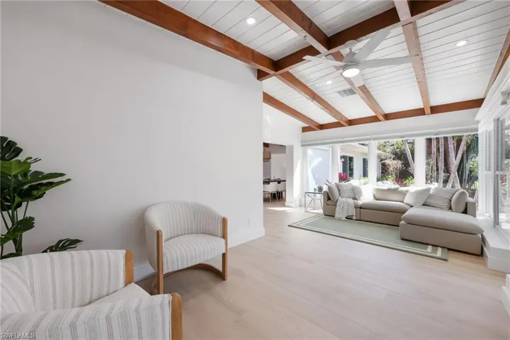Living room with light wood finished floors, visible vents, baseboards, lofted ceiling with beams, and ceiling fan