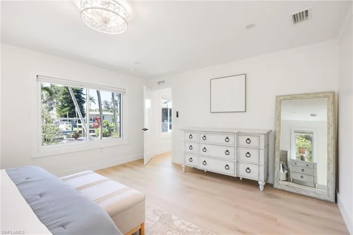 Bedroom with light wood-type flooring, visible vents, crown molding, and multiple windows