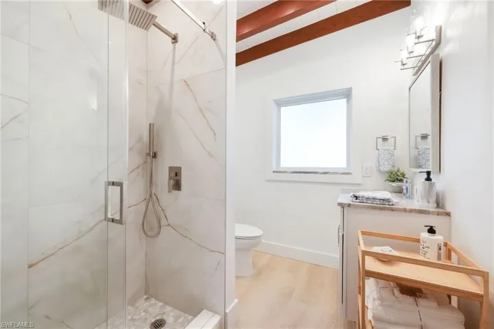Full bath featuring toilet, a marble finish shower, wood finished floors, and vanity