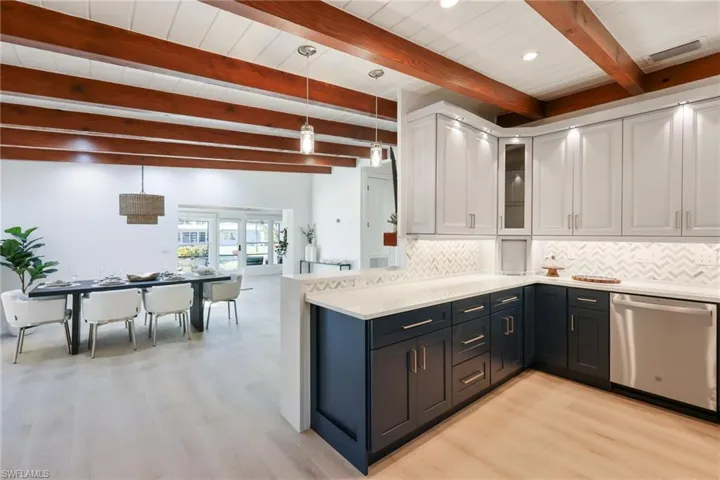 Kitchen featuring decorative backsplash, light countertops, stainless steel dishwasher, and white cabinetry