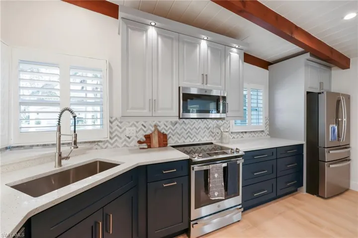 Kitchen with stainless steel appliances, decorative backsplash, white cabinets, a sink, and beamed ceiling