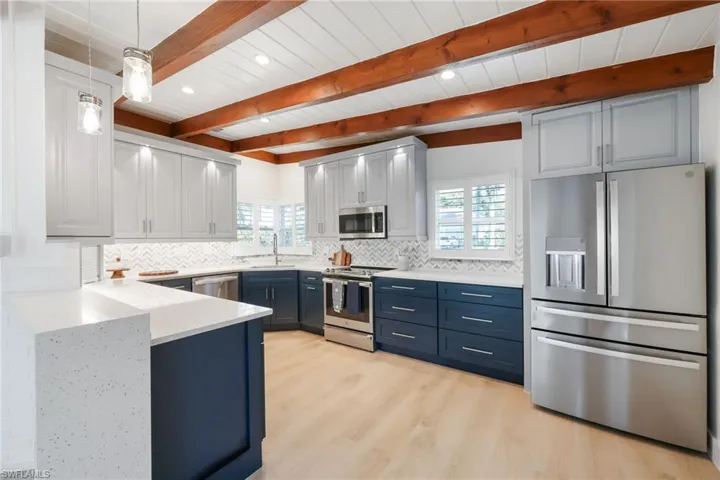 Kitchen with blue cabinets, a peninsula, a sink, appliances with stainless steel finishes, and backsplash