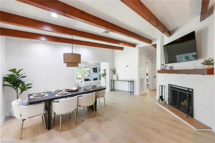 Dining space featuring visible vents, a brick fireplace, wood finished floors, beamed ceiling, and baseboards