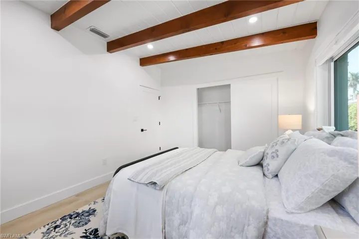 Bedroom with beam ceiling, light wood finished floors, a closet, visible vents, and baseboards