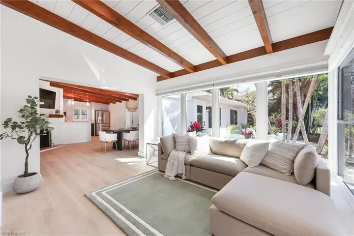 Living area with vaulted ceiling with beams, plenty of natural light, wood finished floors, and visible vents