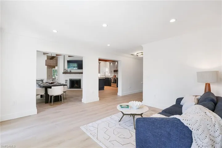 Living room with a fireplace with raised hearth, recessed lighting, light wood-type flooring, and crown molding