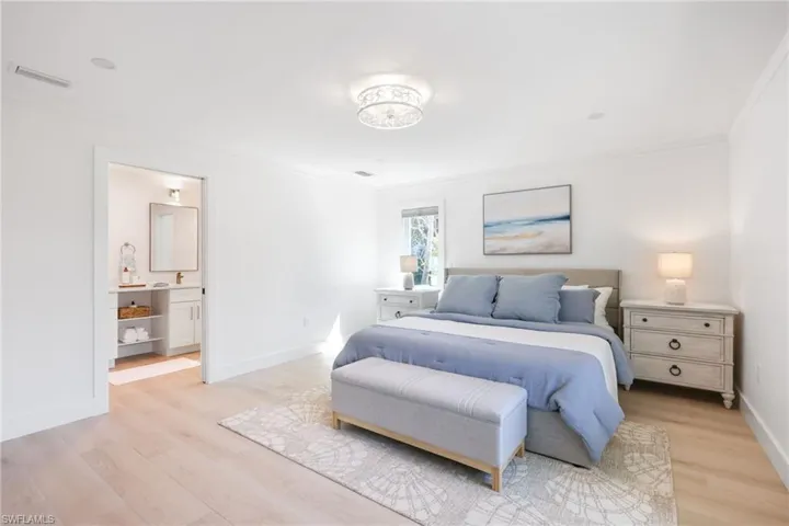 Bedroom featuring visible vents, baseboards, light wood-style flooring, ensuite bathroom, and crown molding
