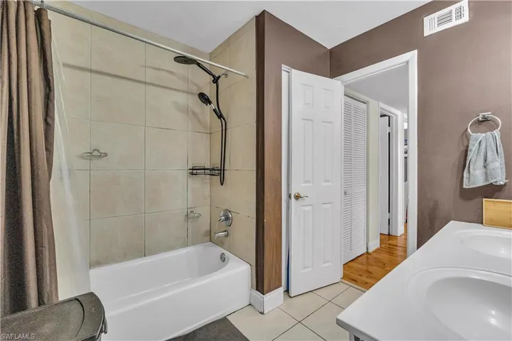 Bathroom featuring shower / bath combination with curtain, double vanity, and light tile patterned floors