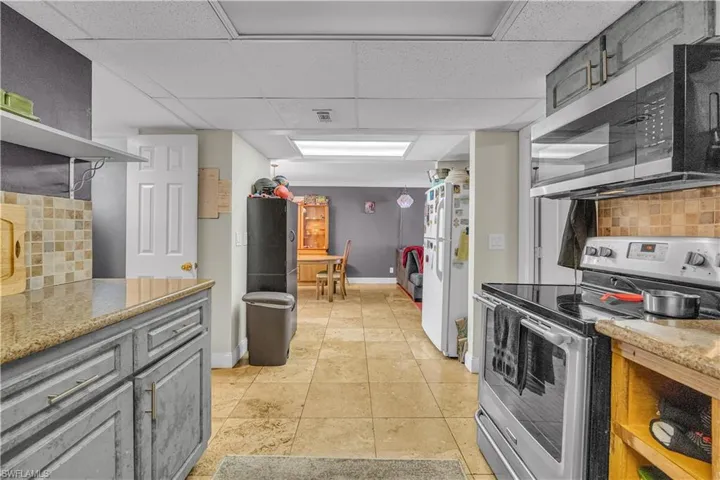 Kitchen featuring backsplash, stainless steel appliances, gray cabinetry, open shelves, and light stone counters