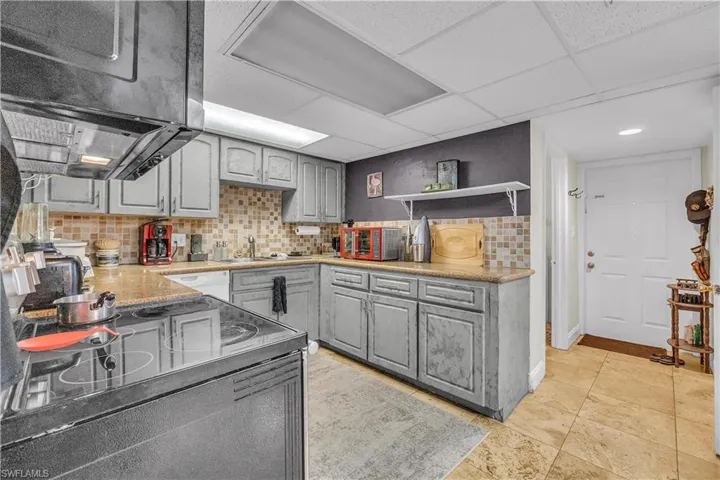 Kitchen featuring black appliances, gray cabinets, open shelves, backsplash, and exhaust hood