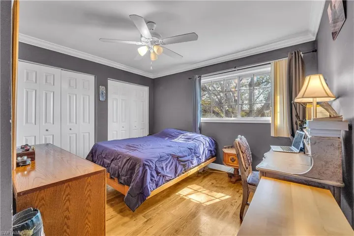 Bedroom with ornamental molding, multiple closets, light wood-style floors, and a ceiling fan