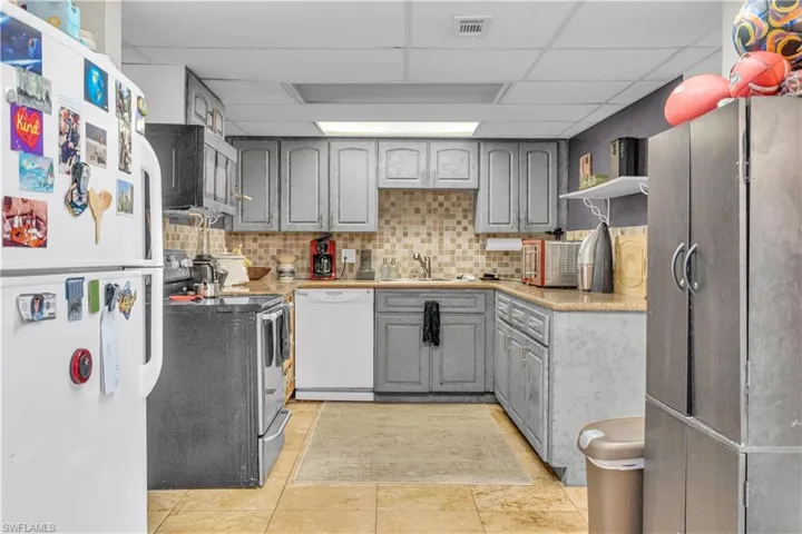 Kitchen featuring gray cabinetry, stainless steel appliances, light countertops, a drop ceiling, and backsplash