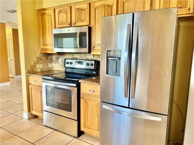 Kitchen featuring tasteful backsplash, light tile patterned floors, dark stone counters, and appliances with stainless steel finishes