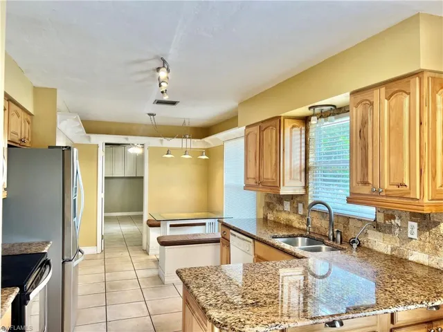 Kitchen with kitchen peninsula, light stone countertops, tasteful backsplash, stainless steel appliances, and sink