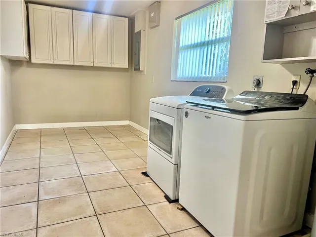 Washroom with cabinets, light tile patterned floors, washing machine and dryer, and electric panel