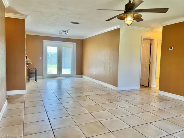 Empty room with ceiling fan, french doors, light tile patterned floors, and ornamental molding