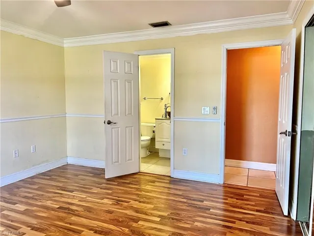 Unfurnished bedroom featuring hardwood / wood-style flooring, ceiling fan, ornamental molding, and connected bathroom