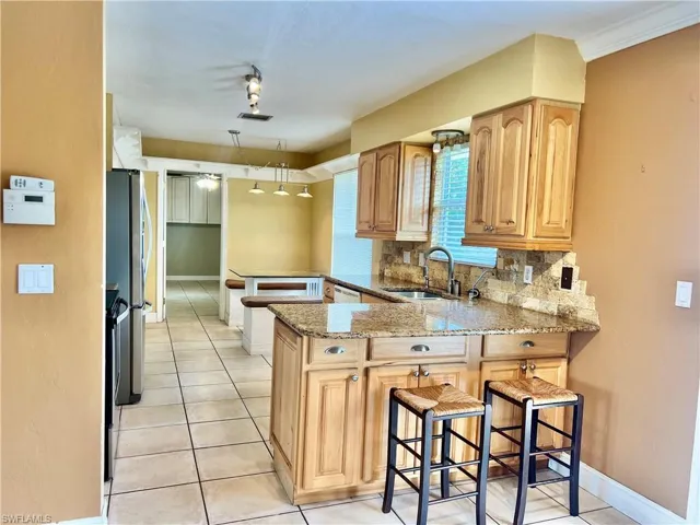 Kitchen featuring a kitchen bar, sink, tasteful backsplash, light stone counters, and kitchen peninsula