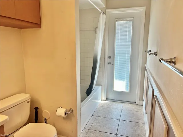 Bathroom featuring tile patterned flooring, shower / bathtub combination with curtain, and toilet