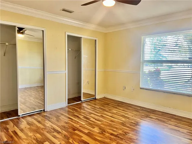 Unfurnished bedroom featuring wood-type flooring, multiple closets, ceiling fan, and ornamental molding