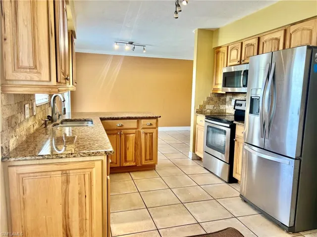 Kitchen with light stone countertops, appliances with stainless steel finishes, track lighting, sink, and light tile patterned floors