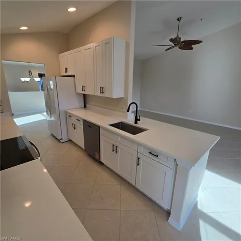 Kitchen with lofted ceiling, white cabinetry, light tile patterned flooring, black appliances, and a peninsula