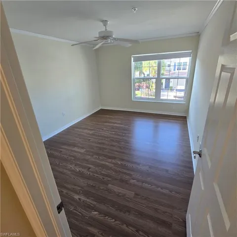 Empty room featuring ornamental molding, dark wood-style floors, and a ceiling fan