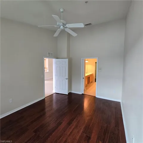 Empty room featuring a towering ceiling, dark wood-style flooring, and a ceiling fan