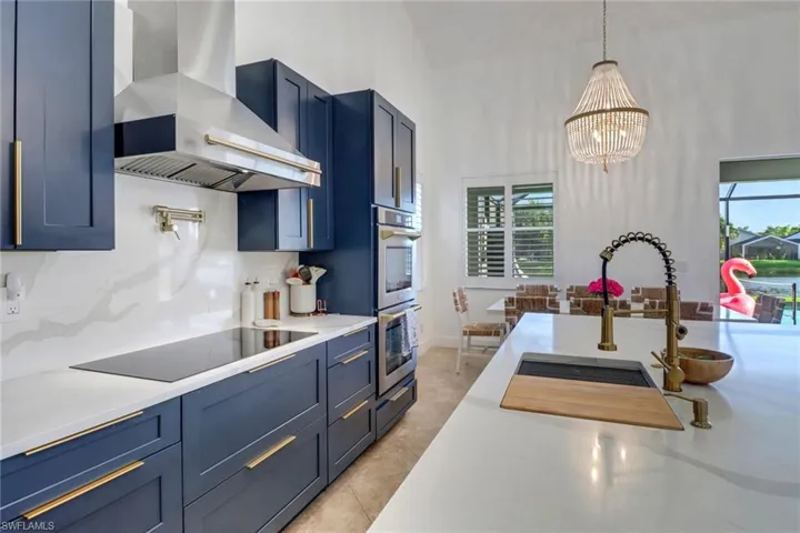Kitchen with stainless steel double oven, hanging light fixtures, black electric stovetop, a chandelier, and wall chimney exhaust hood