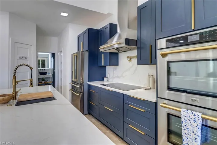 Kitchen with wall chimney range hood, light stone counters, appliances with stainless steel finishes, a sink, and blue cabinets