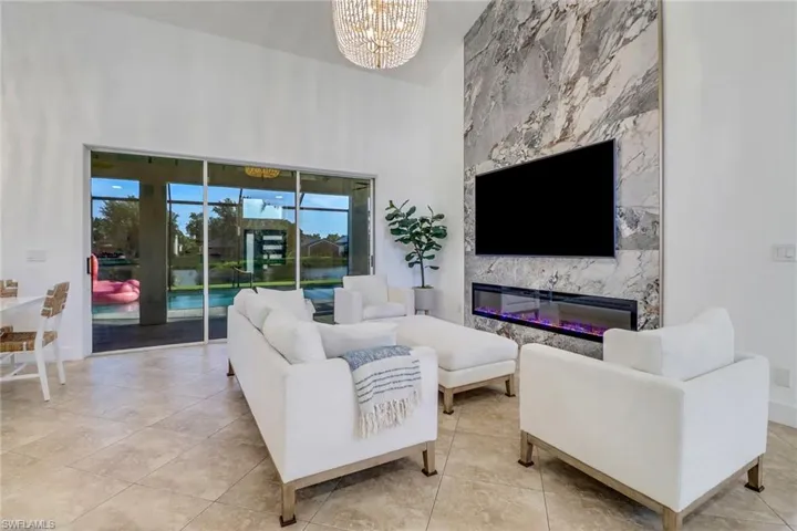 Living room with an inviting chandelier, tile patterned flooring, a towering ceiling, baseboards, and a high end fireplace