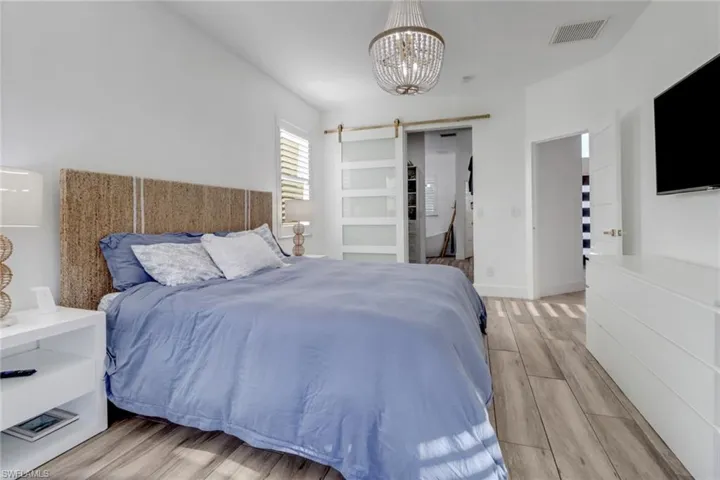 Bedroom featuring visible vents, a barn door, light wood-style flooring, and a notable chandelier
