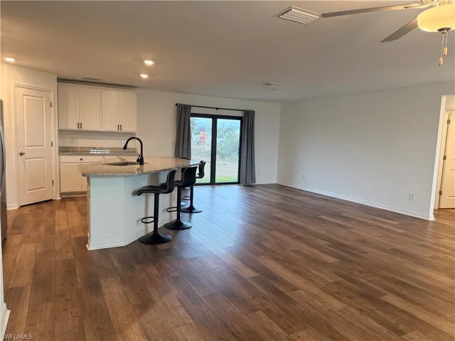 Kitchen featuring light stone countertops, white cabinetry, open floor plan, a kitchen breakfast bar, and dark wood finished floors