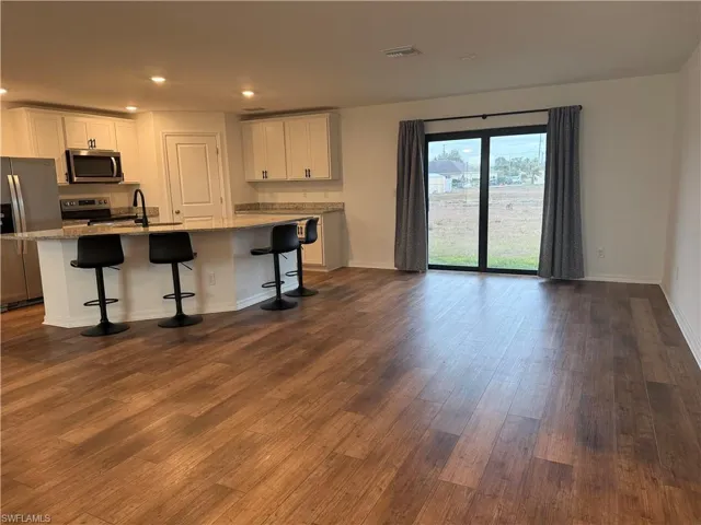 VIEW FROM FRONT DOOR - Kitchen featuring stainless steel appliances, a kitchen bar, a kitchen island with sink, white cabinets, and light stone countertops