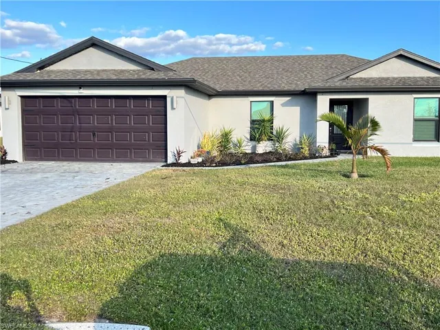 Ranch-style home with stucco siding, a front yard, roof with shingles, and decorative driveway