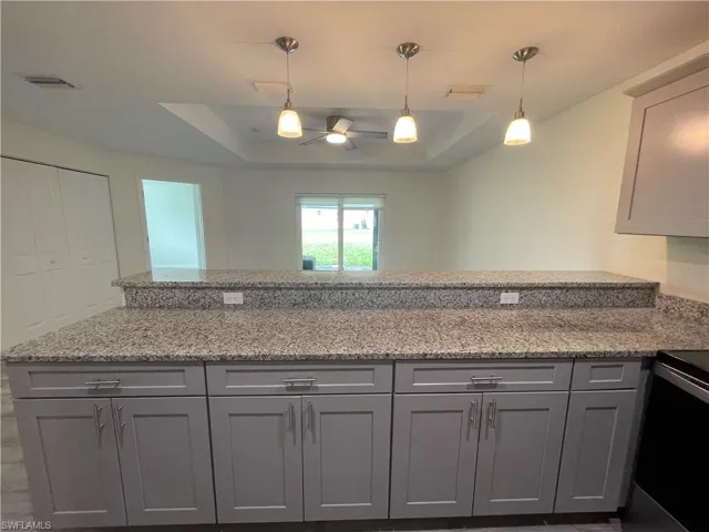 Kitchen with light stone counters, electric stove, decorative light fixtures, and gray cabinetry