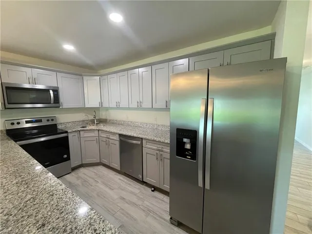 Kitchen featuring sink, stainless steel appliances, light wood-type flooring, and light stone countertops