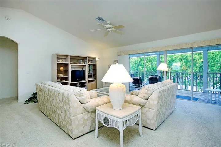 Living area featuring ceiling fan, high vaulted ceiling, carpet, arched walkways, and visible vents