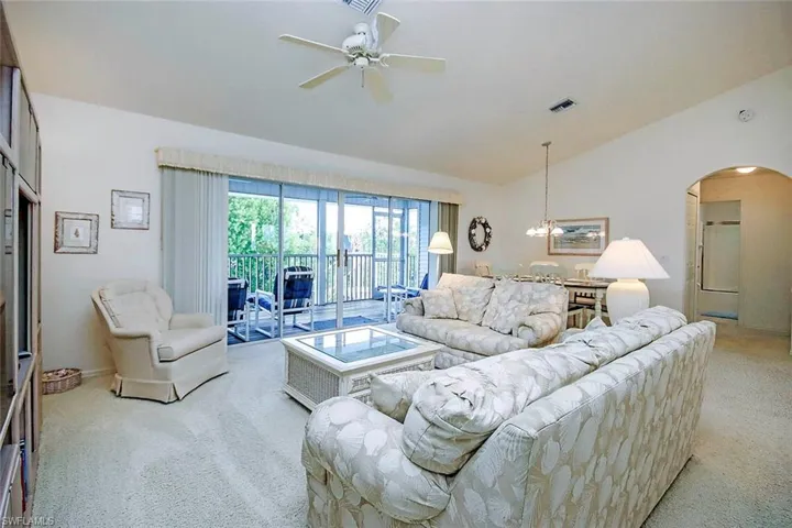 Living room featuring visible vents, arched walkways, ceiling fan with notable chandelier, light carpet, and lofted ceiling