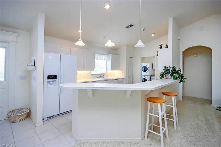 Kitchen featuring visible vents, white cabinets, white fridge with ice dispenser, a kitchen bar, and stacked washer and dryer