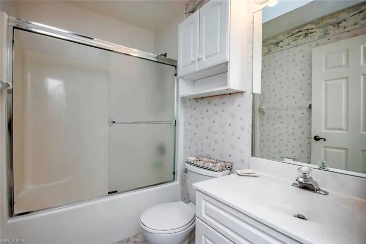 Bathroom featuring bath / shower combo with glass door, vanity, wallpapered walls, and toilet