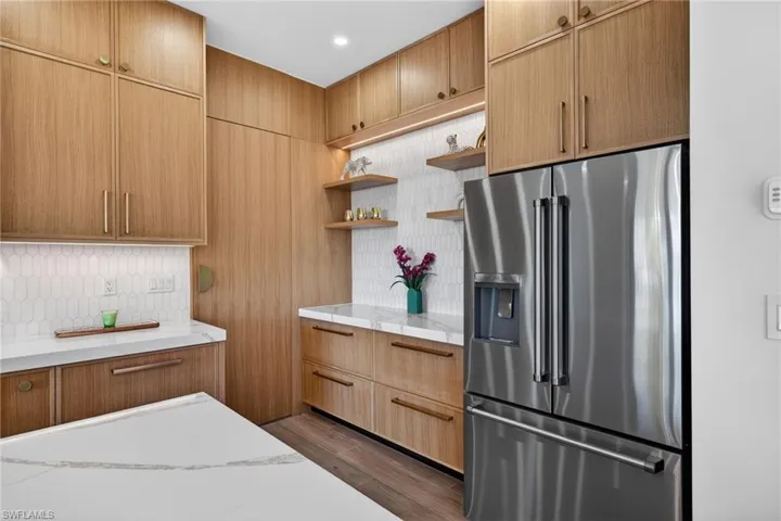 Kitchen with high quality fridge, open shelves, dark wood-style floors, tasteful backsplash, and light stone counters
