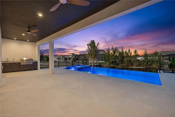 Pool at dusk featuring area for grilling, a pool with connected hot tub, and a patio area