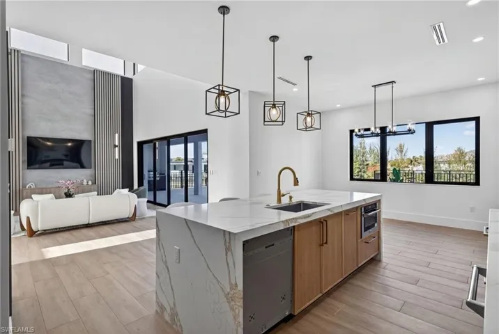 Kitchen featuring light stone counters, open floor plan, a center island with sink, and wood finish floors