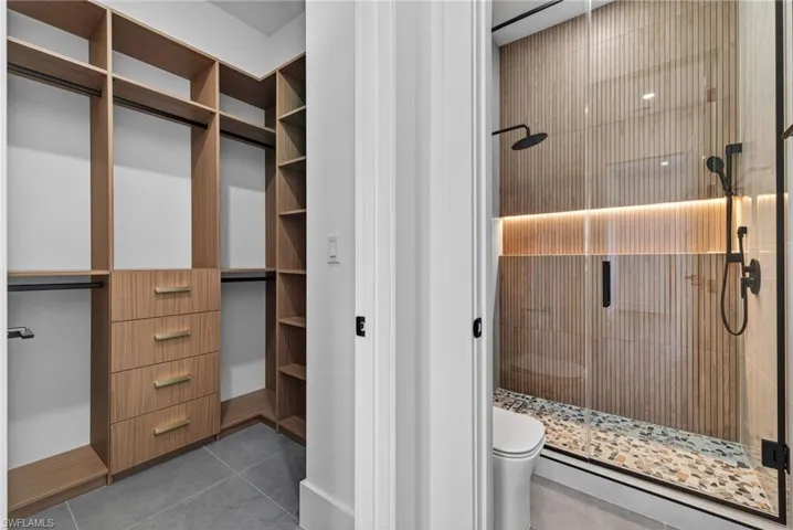 Full bath featuring a shower stall, light tile patterned flooring, and a spacious closet