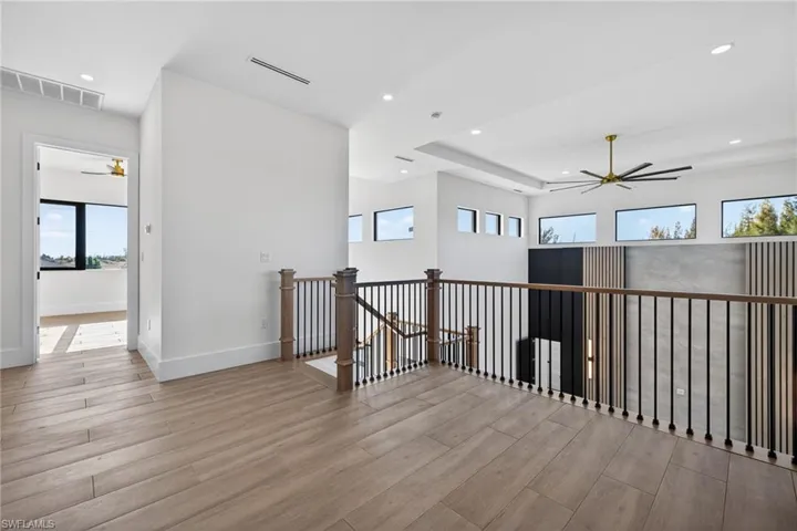 Hallway with an upstairs landing, light wood-style floors, and recessed lighting