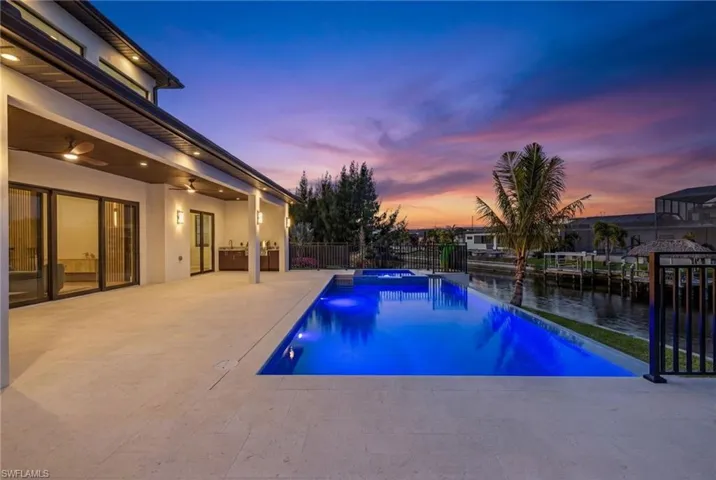 Pool at dusk featuring a patio, a pool with connected hot tub, a fenced backyard, and a water view
