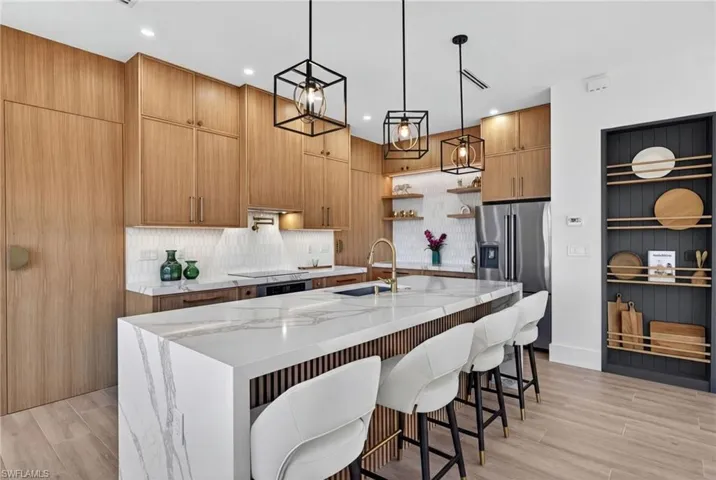Kitchen featuring light stone counters, wood tiled floors, an island with sink, and stainless steel appliances