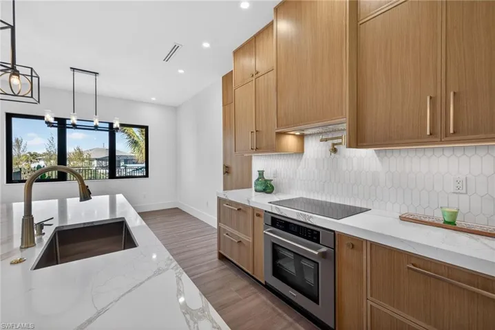 Kitchen with light stone countertops, oven, dark wood-style floors, suspended lighting, and backsplash