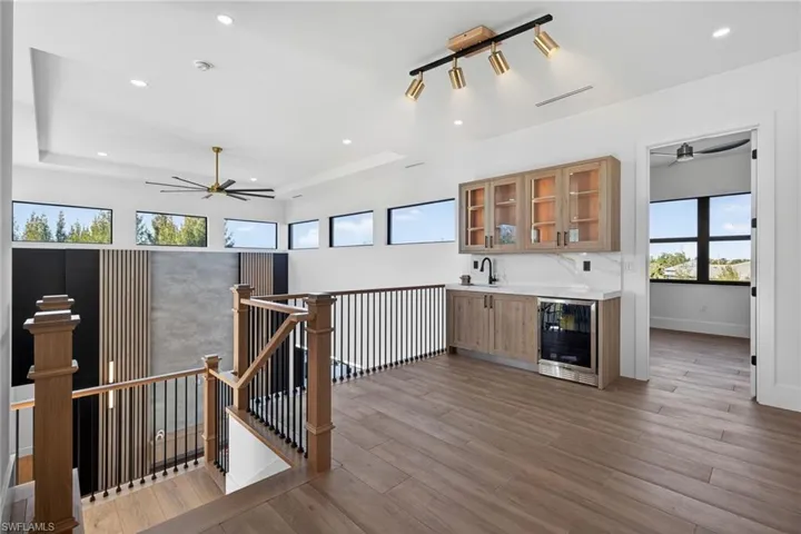 Indoor wet bar with a ceiling fan, glass insert cabinets, wine cooler, light wood-style floors, and light countertops